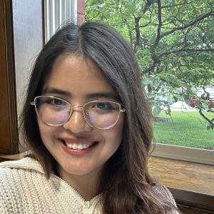 Denisse Ramos Guzman smiling in front of a window wiht a tree in the background.