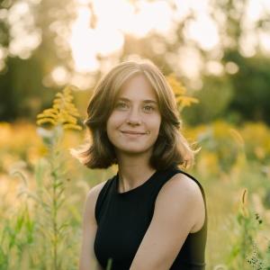 Kelsey Wegner smiling while sitting on the grass in front of trees. 