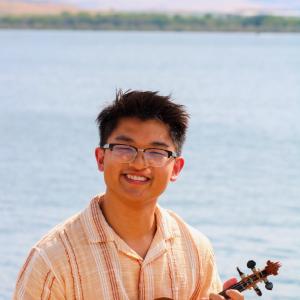 Quinton Kuhn smiling and playing an instrument in front of a body of water.