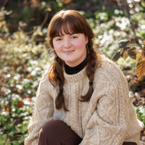 Anja Caverley-Light smiling while sitting in a field of grass and flowers.