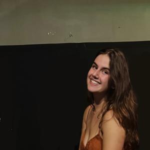 Beatriz Vasconcellos Neumann smiling in front of a black and white background.
