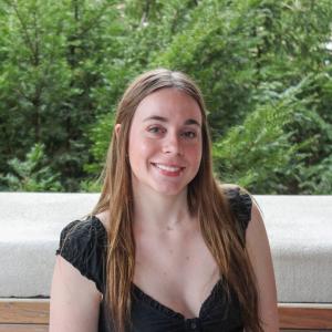 Brooklyn Sims sitting on a park bench in front of trees, smiling.