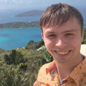 Nathan Koedyker smiling in front of greenery and water.
