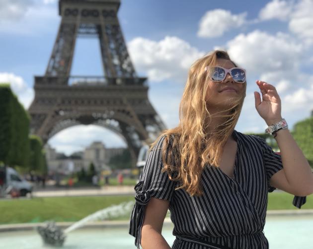 a student adjusting her sunglasses in front of the Eiffel Tower on a sunny summer day