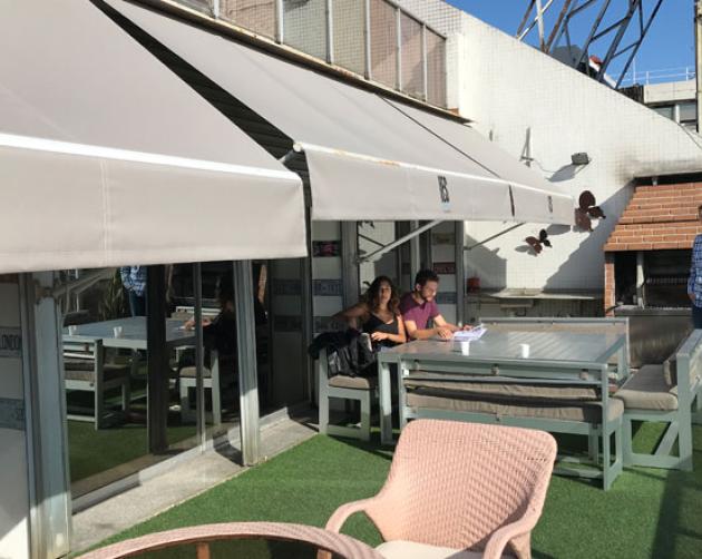 A view of an outdoor patior. The tan awnings display the IES Abroad Buenos Aires logo. Three people gather around a table at the far end of the patio.