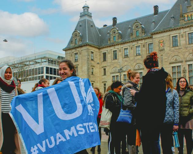 Students celebrating outside on Vrije Universiteit's campus. One student is wearing a blue VU flag.