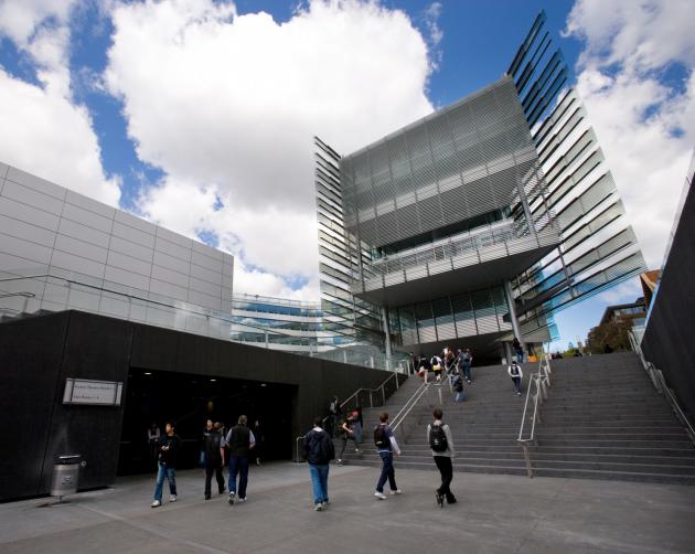 Students on their way to classes on University of Auckland's campus, surrounded by modern, gray architecture.
