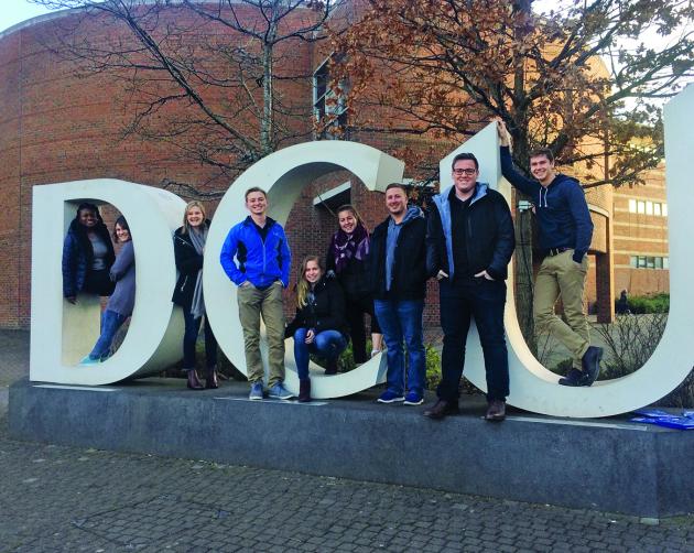 Students stand on Dublin City University's giant letter display. The letters are "DCU."