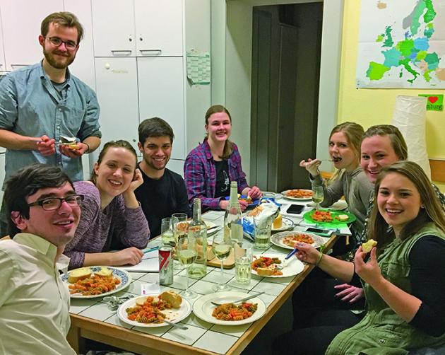 A group of students happily sitting around a dining room table full of food and drinks.