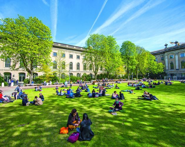 Students sitting on a vibrant green lawn on Humboldt-Universität zu Berlin's campus.