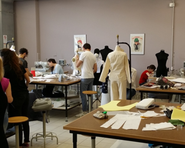 Students create clothing in a classroom with papers and mannequins spread around the room.
