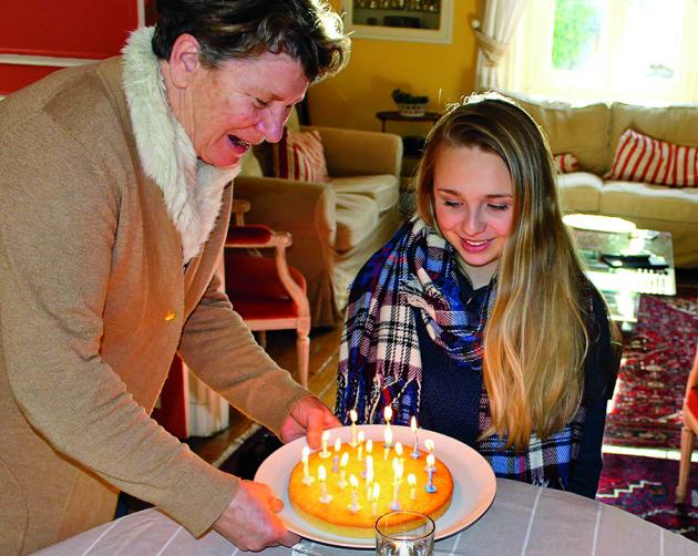 A student's host mother places a birthday cake with candles in front of her in a Nantes homestay.
