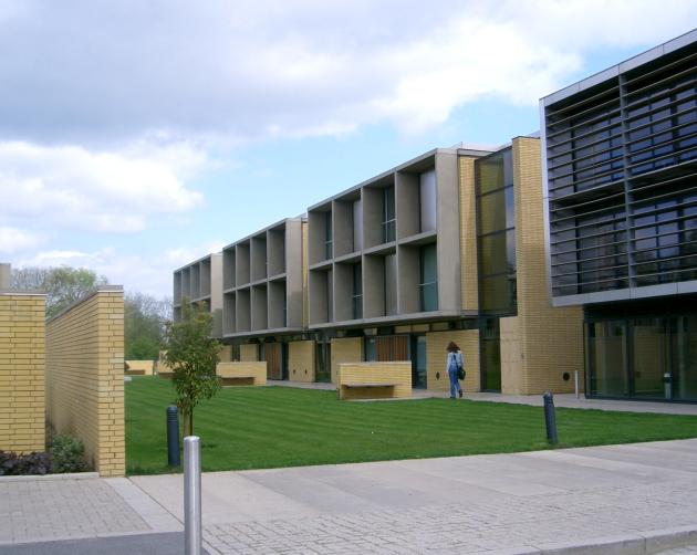 A student walks by rows of modern, square buildings with multiple large windows in Oxford.