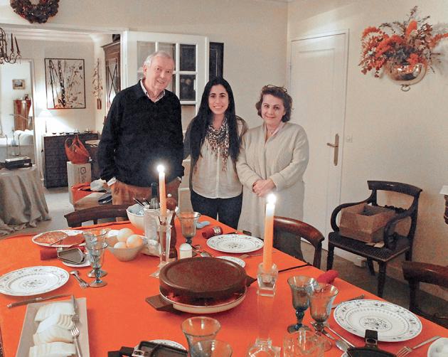 A student with their host parents standing at a set dining room table in a Paris homestay.