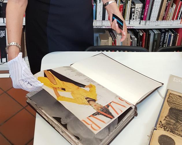 A student flips through a vintage copy of Bazaar magazine wearing protective gloves. 