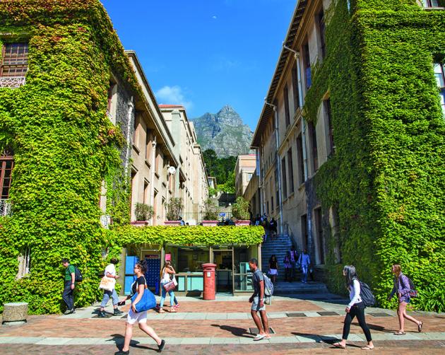 Students walk past buildings covered in lush vegetation on a sunny day at the University of Cape Town.