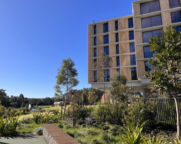a photo of the housing building at Macquarie University in Sydney. A multi-level building with a blue sky and plenty of greenery outside.
