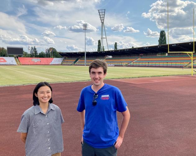 2 students standing in a stadium, with blue sky in the background
