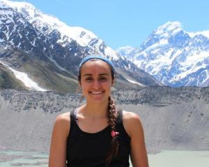 a girl standing with mountain background and smiling at the camera person 