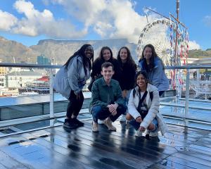 students posing for a picture on a pier. in the background, there is a Ferris wheel and mountains.
