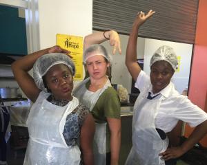 Three students pose in plastic aprons in hats outside of their baking class.