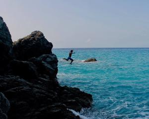 student jumping off rocks into water in Italy.