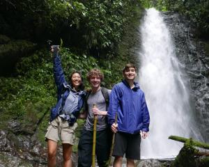 Three students standing in front of a waterfall in the rainforest in Ecuador