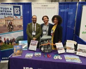 three IES Abroad employees stand in front of a catalog-filled table at a college study abroad fair