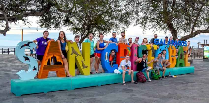 a cohort of students pose for a photo with the San Cristobal Galápagos sign