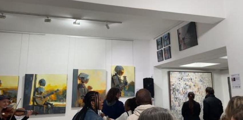 A picture taken at an art gallery featuring multiple pieces of art work and a busy atmosphere. 
