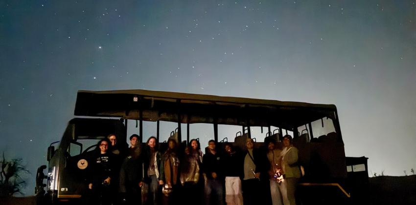 Image of group of people in front of a big vehicle in the night time with the stars.  