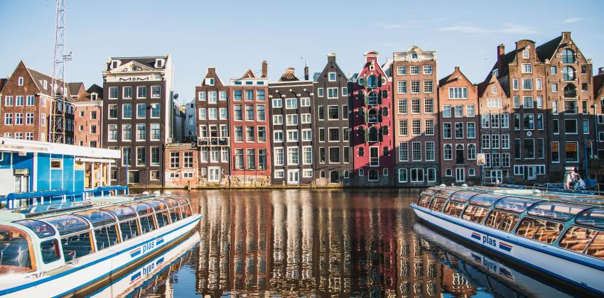 Boats sit in Amsterdam Centraal Canal in front of traditional Amsterdam architecture