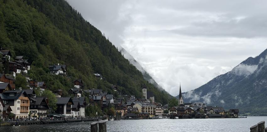 A view of Lake Hallstatt, with houses, mountains covered in fog, and dark water.