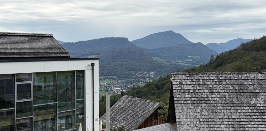 A view from near the salt mine. There is a table with several people eating, a modern building on the left, and a view of mountains in the distance.