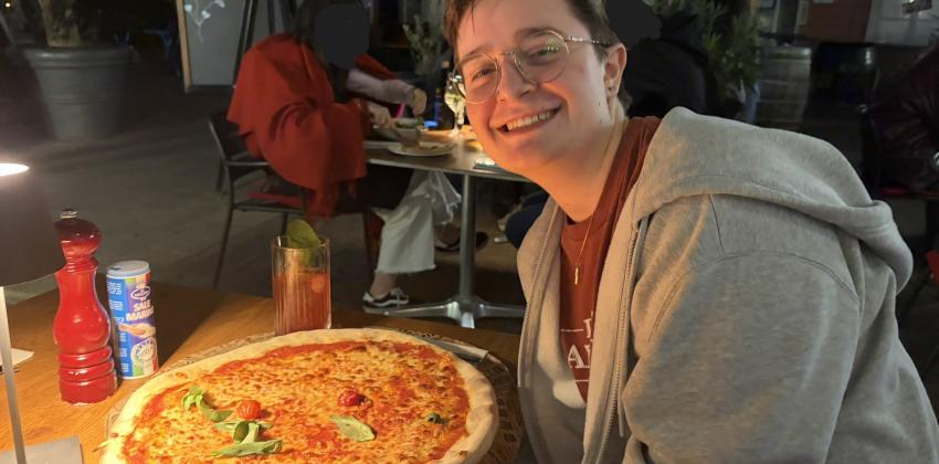 The author smiles and poses with a giant margherita pizza at a restaurant table.