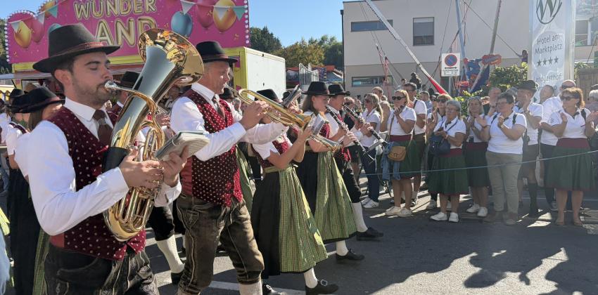 A line of musicians dressed in uniform processes from left to right, while a crowd claps in the background.