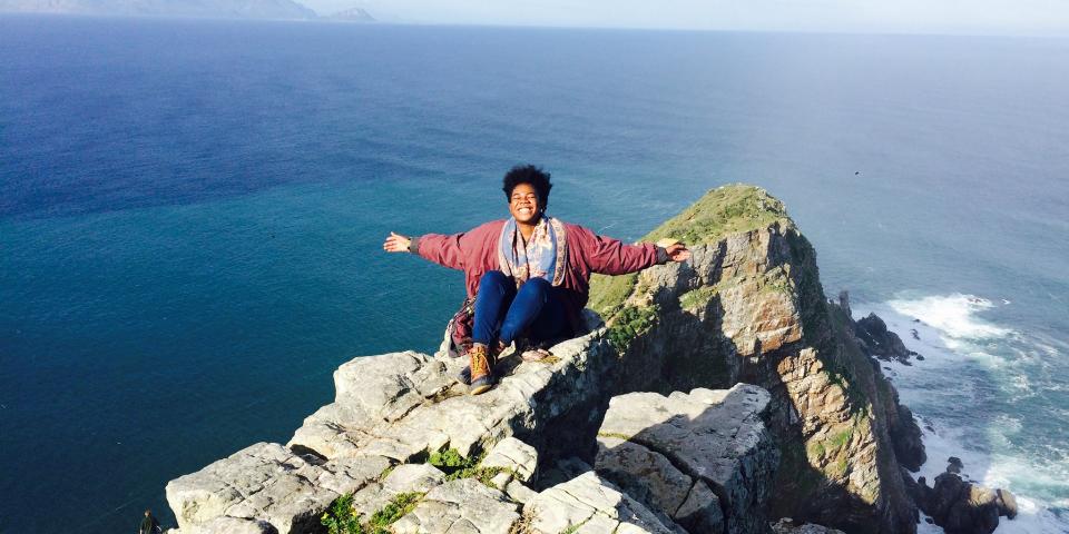 a student sitting on a mountaintop by the ocean