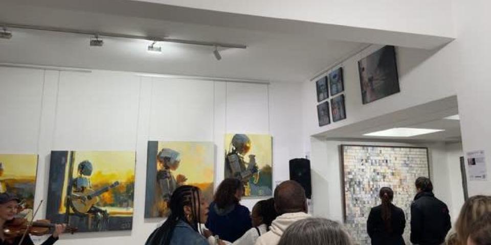 A picture taken at an art gallery featuring multiple pieces of art work and a busy atmosphere. 