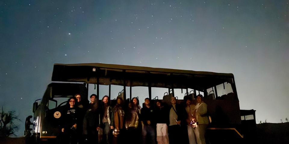 Image of group of people in front of a big vehicle in the night time with the stars.  